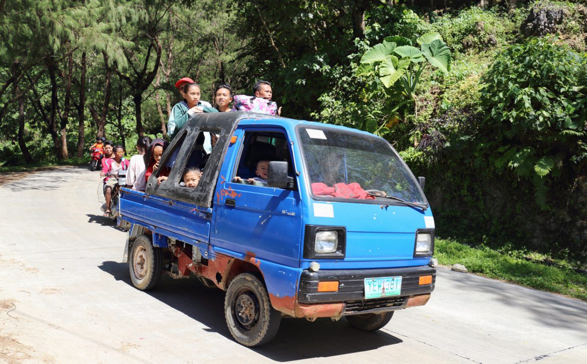 Several people riding a small blue truck in the mountains.