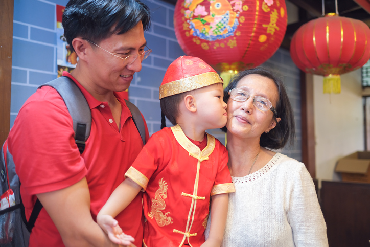 Grandparents and grandson wearing Chinese traditional clothing as grandson kisses grandma's cheek.