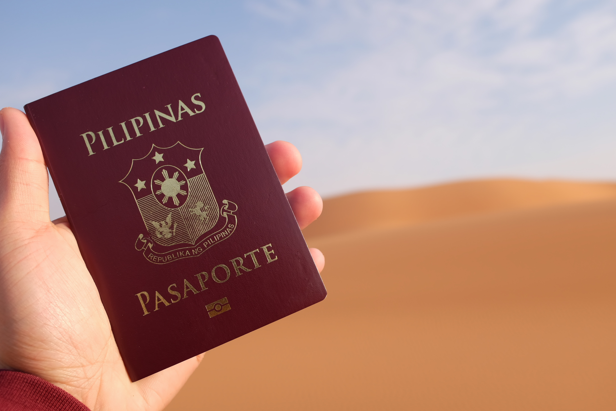 Hand holding up a Philippine passport in a desert.