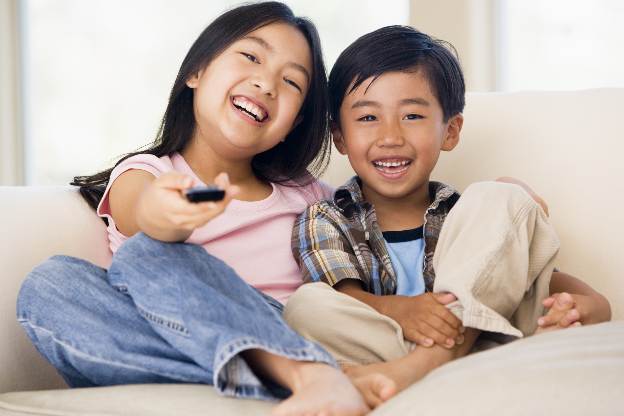 A girl and boy sat on couch happily watching TV