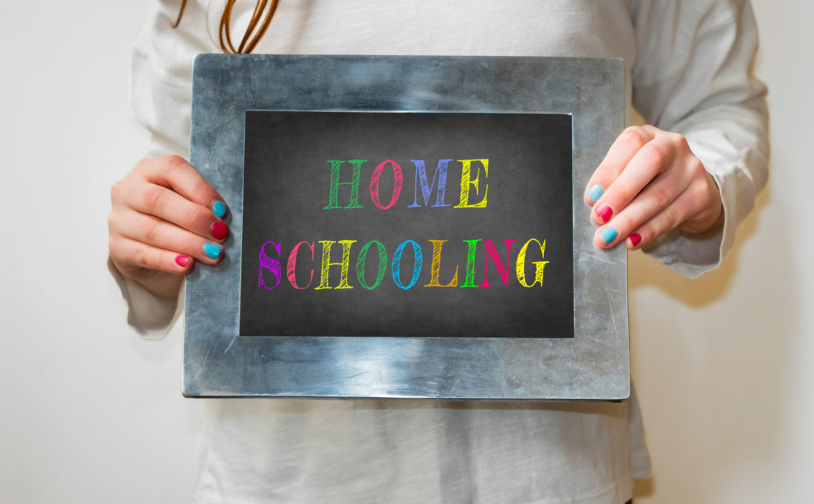 Girl holding up a small blackboard with colourful writing of "Home Schooling"