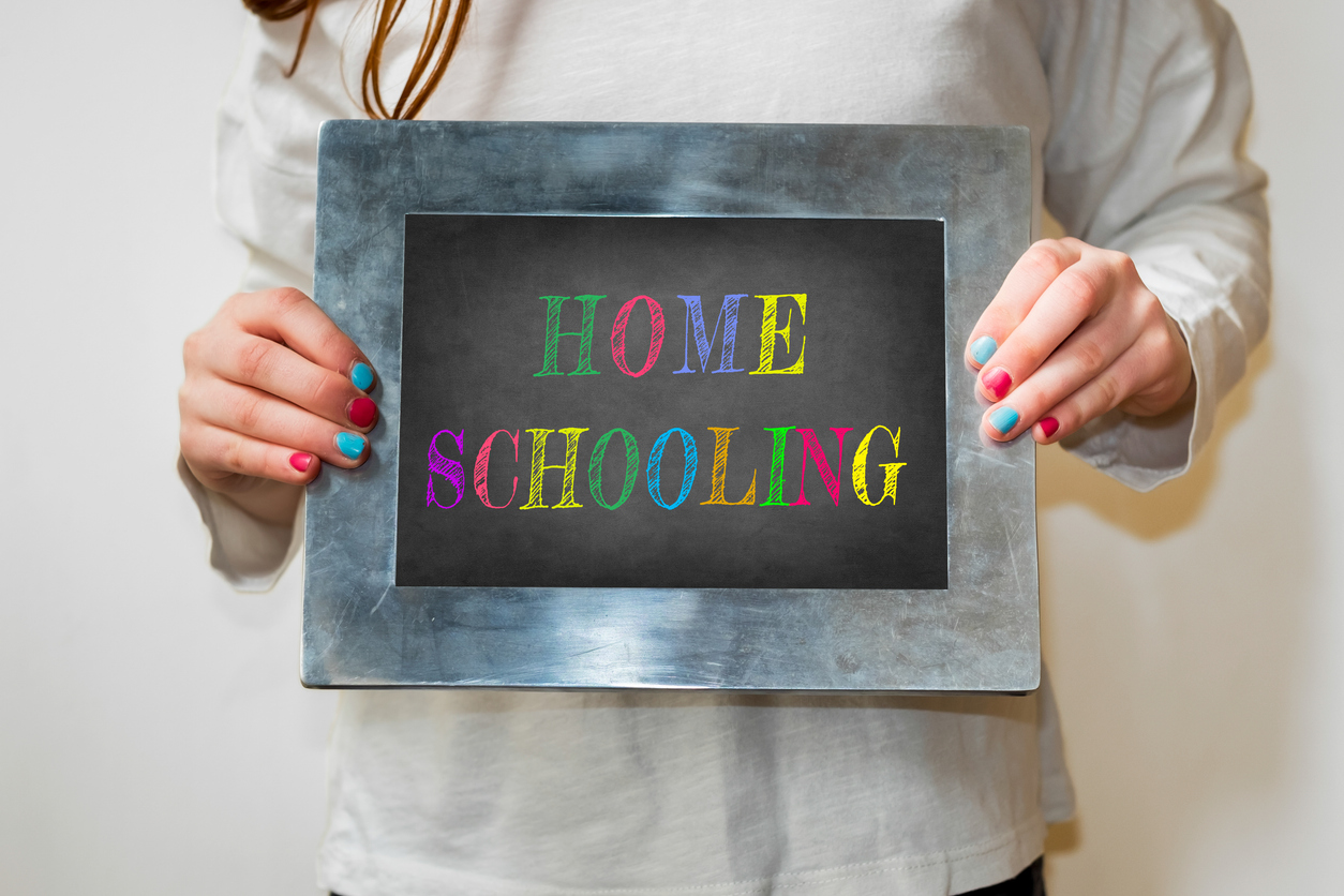 Girl holding up a small blackboard with colourful writing of "Home Schooling"
